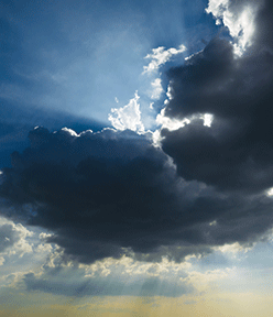 Dramatic sky with sunbeams breaking through dark clouds during sunset, creating a beautiful and moody atmosphere.