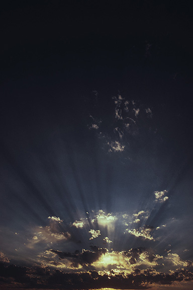 Sunset with dramatic clouds and sun rays breaking through, creating a serene and picturesque evening sky.