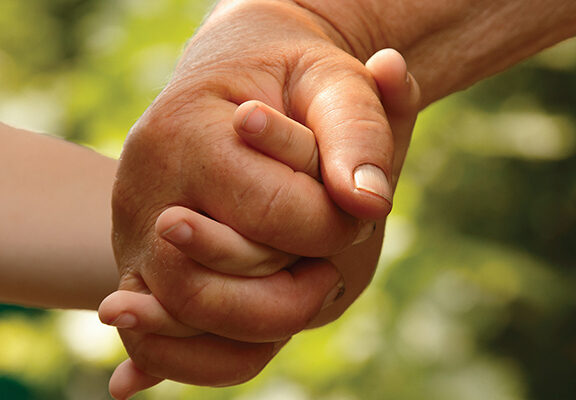 Elderly and young hands holding, symbolizing connection and care against a blurred green background.