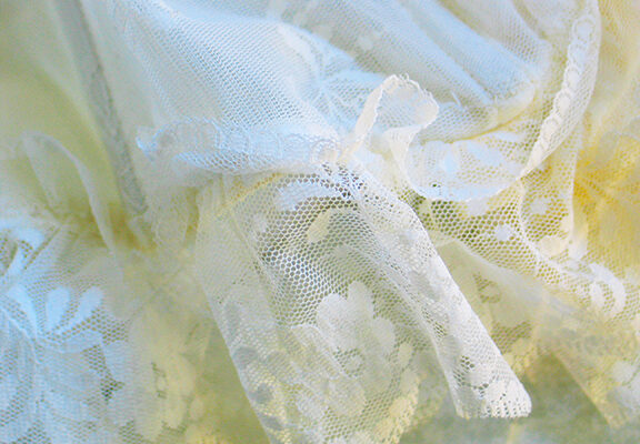 Delicate white lace fabric with floral patterns, draped elegantly in soft folds, highlighting intricate embroidery.