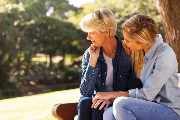 Two women sitting together on a bench in a park, expressing support and comfort to each other in a serene outdoor setting.
