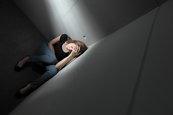A person sitting in a corner under dramatic lighting, expressing stress or contemplation.