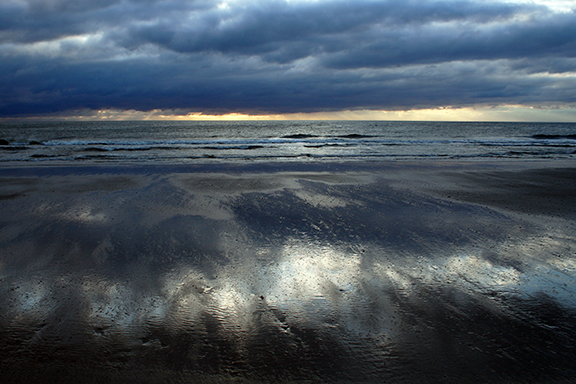 Moody beach at sunrise with dark clouds and reflective wet sand capturing the serene beauty of a coastal morning.
