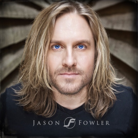 Portrait of a person with long blonde hair and blue eyes, set against a neutral background.