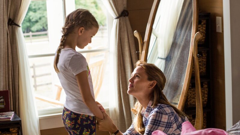 Mother and daughter share a heartfelt moment by a window, holding hands and smiling warmly.