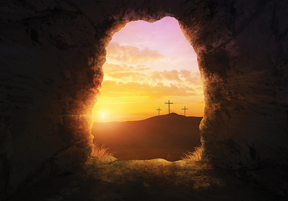 Sunrise view from a cave overlooking three crosses on a hill, symbolizing resurrection and hope.