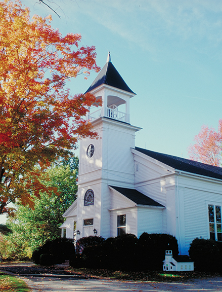 White church with steeple amidst autumn trees and clear sky, showcasing serene fall scenery.