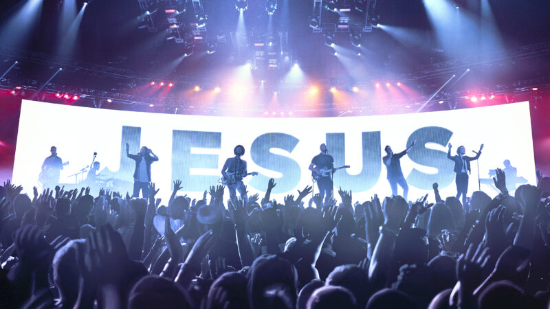Concert scene with a band on stage, vibrant lights, and Hillsong: Let Hope Rise text displayed.