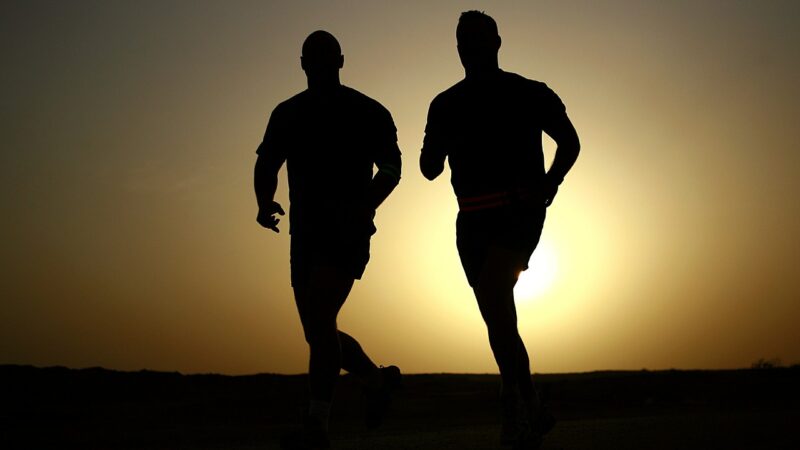 Silhouettes of two runners jogging at sunset, against a golden sky.