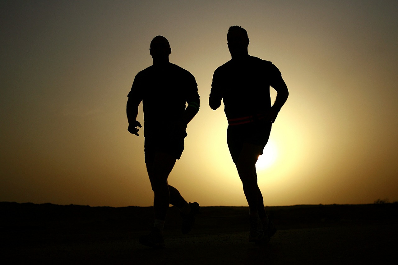 Silhouettes of two runners jogging at sunset, against a golden sky.