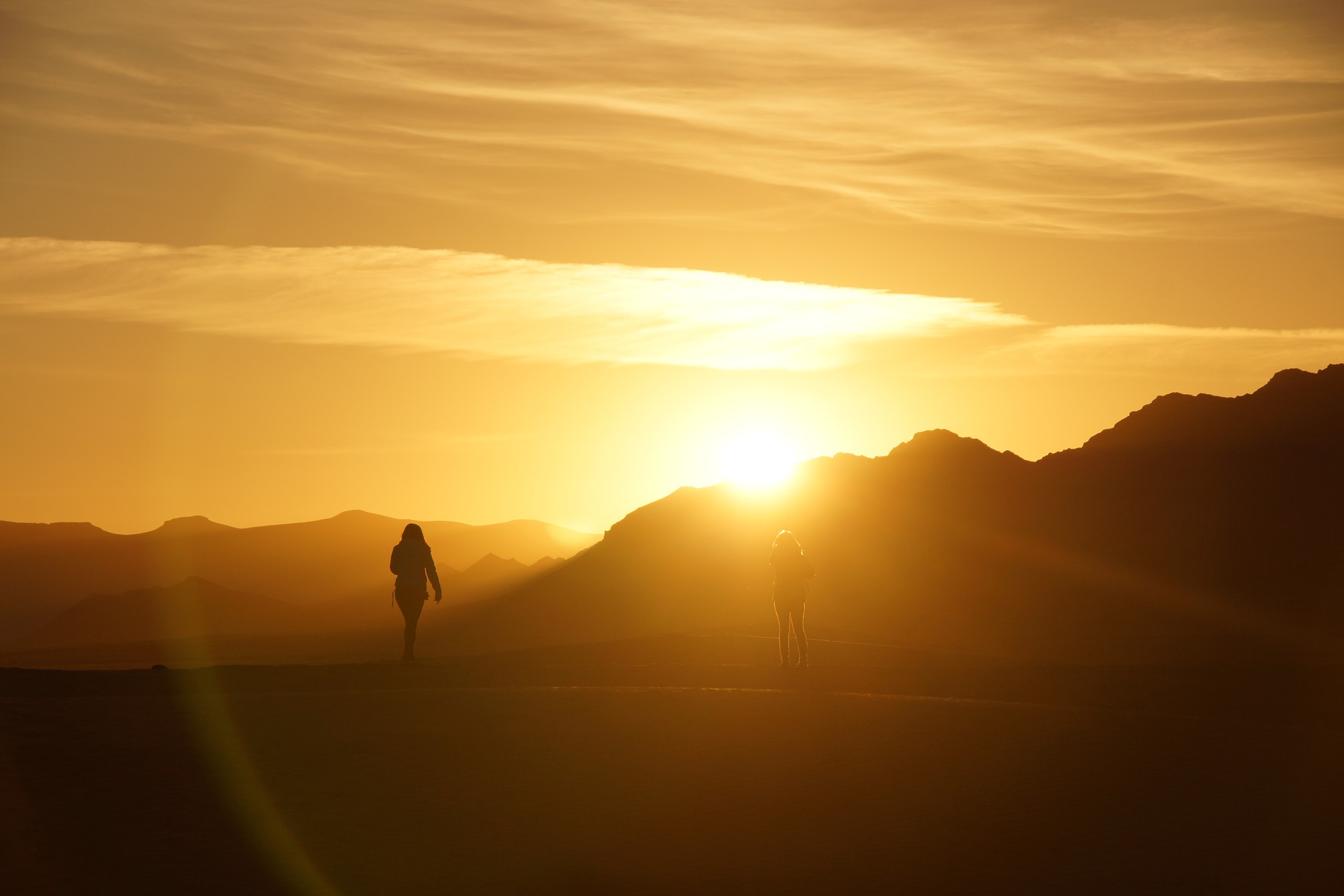 Silhouetted hikers at sunrise on a mountain trail, surrounded by glowing golden light.