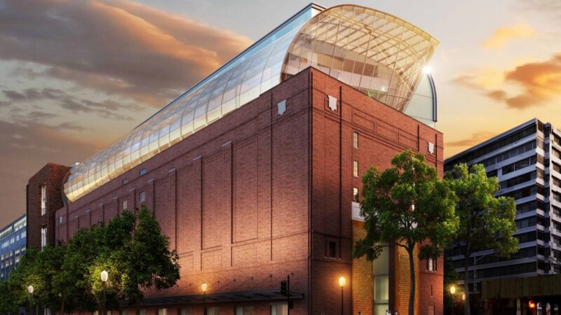 Modern museum with a glass dome extension on a historic brick building at sunset.