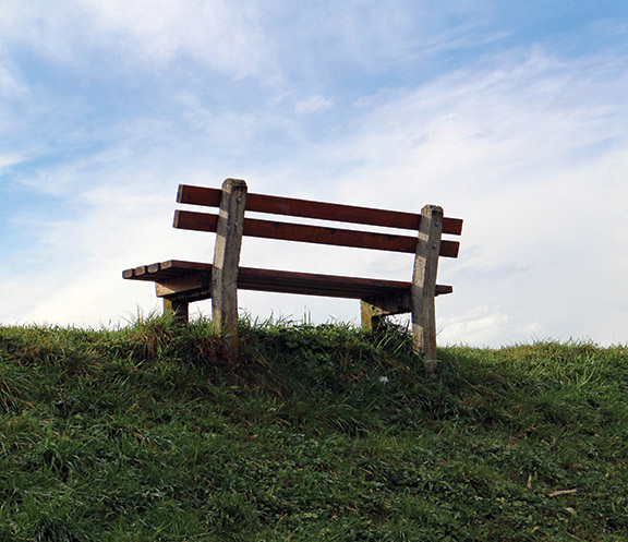 Wooden bench on grassy hill under blue sky, ideal for relaxation and nature enjoyment.
