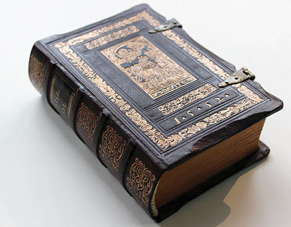 Antique leather-bound book with intricate gold detailing and metal clasps on white background.
