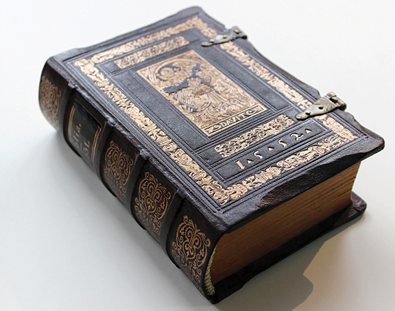 Antique leather-bound book with intricate gold detailing and metal clasps on white background.