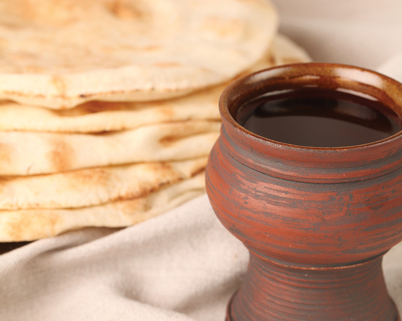 Clay mug of dark beverage beside a stack of flatbread on a beige cloth.