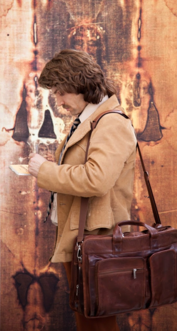 Person reading notes, carrying a leather bag, in front of a vintage, patterned background.