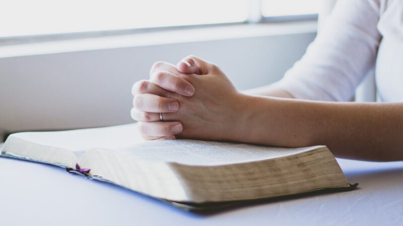 Hands clasped in prayer over an open book, symbolizing faith and reflection.