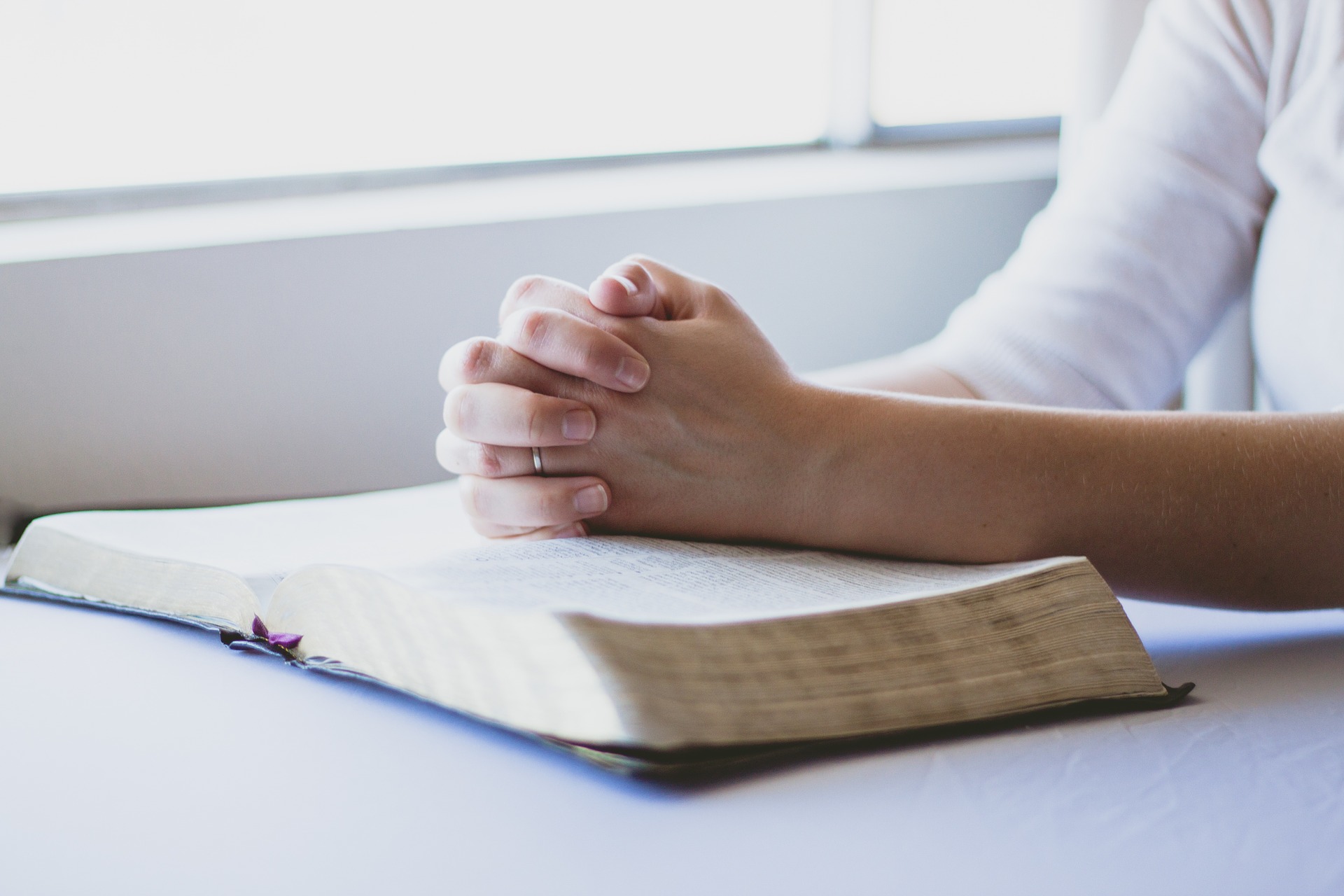 Hands clasped in prayer over an open book, symbolizing faith and reflection.