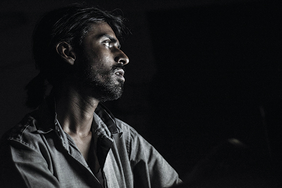 Dark, moody portrait of a man gazing into the distance with dramatic lighting.