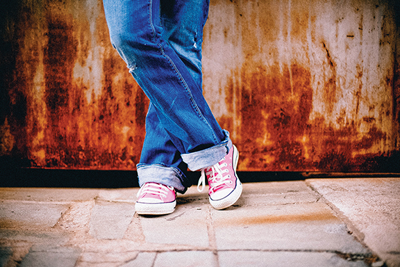 Casual style with rolled-up jeans and pink sneakers against a rusty backdrop. Urban fashion statement.