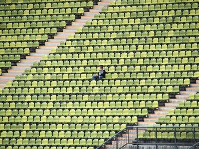 Empty stadium seats with one person sitting, highlighting solitude and spaciousness in green and yellow tones.