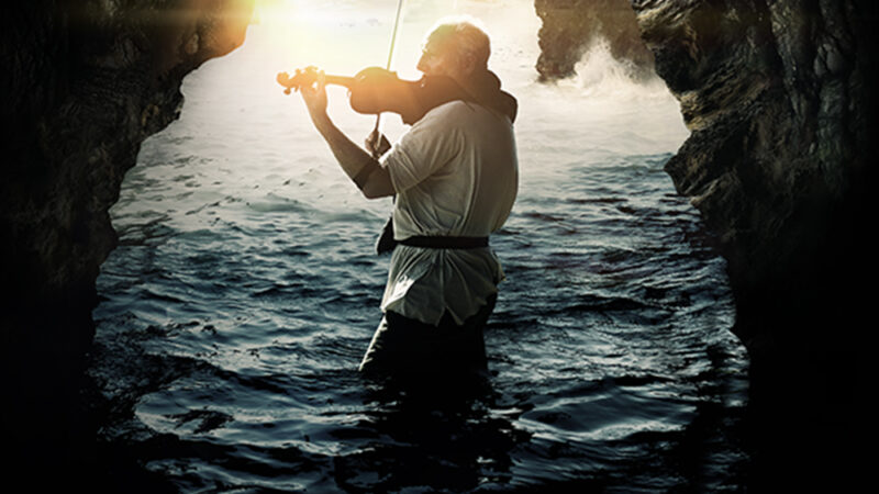 Violinist playing in a scenic cave by the sea at sunset, promotional image for The Heart of Man film.