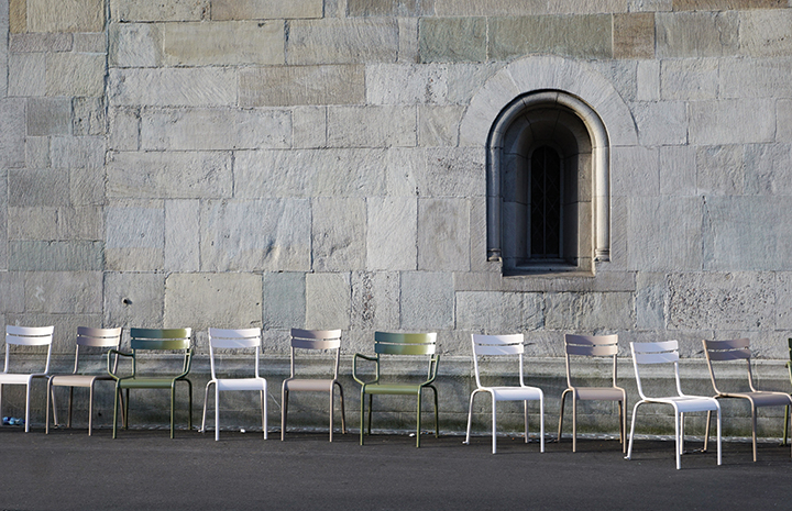Empty chairs aligned against a stone wall with an arched window.
