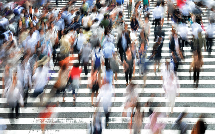 Blurred image of people crossing a busy street at a zebra crossing, capturing urban hustle and movement.