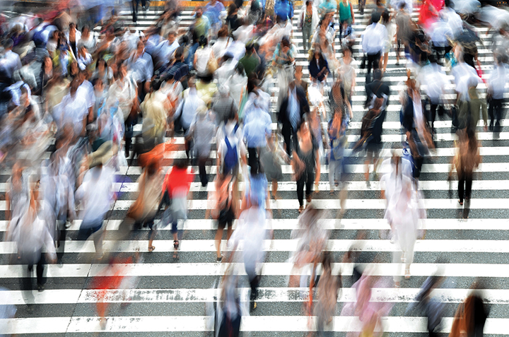 Blurred image of people crossing a busy street at a zebra crossing, capturing urban hustle and movement.