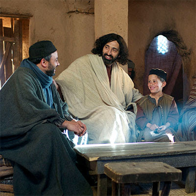 Three people in historical costumes sharing a joyful moment indoors, with light streaming through a window.