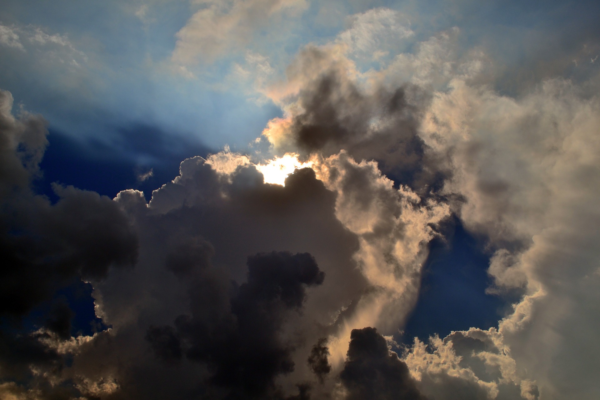 Dramatic cloudy sky with sun rays peeking through dark clouds, creating a stunning natural contrast and light effect.