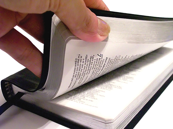 Hand flipping pages of an open Bible with black cover, showcasing text and chapters.