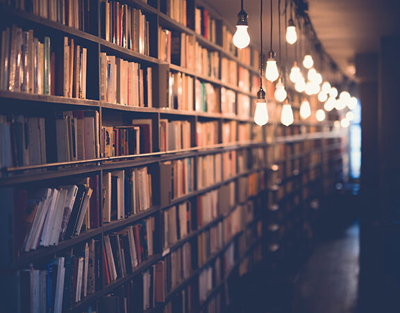 Bookshelves in a dimly-lit library with hanging lights creating a cozy atmosphere.