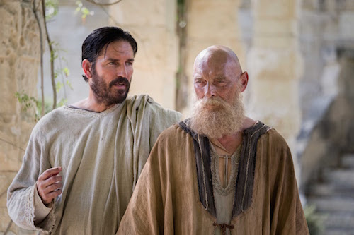 Two men in biblical costumes talking in an ancient stone setting, one with a beard and the other gesturing.
