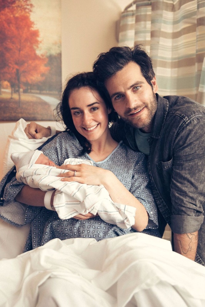 Smiling couple with newborn in hospital bed, symbolizing family joy and new beginnings.
