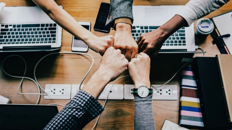 Team fist bump over laptops symbolizing collaboration and unity in a modern office setting.