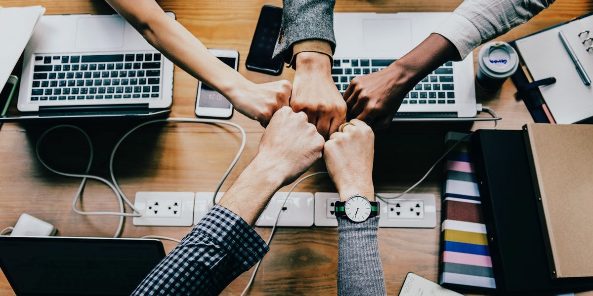 Team fist bump over laptops symbolizing collaboration and unity in a modern office setting.