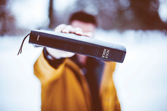 Person holding out a Bible in a snowy landscape, emphasizing faith and spirituality in a peaceful winter setting.