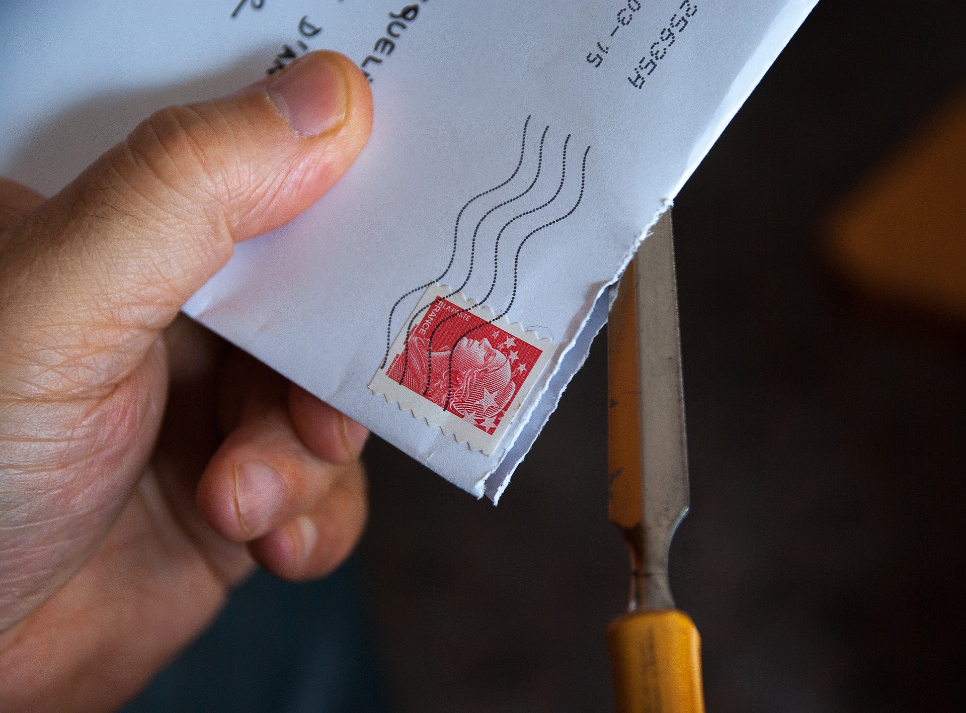 Person opening an envelope with a red postage stamp using a tool for mail processing.