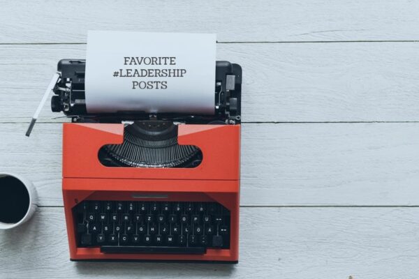 Red typewriter with paper displaying Favorite #Leadership Posts next to a coffee cup on a wooden table.