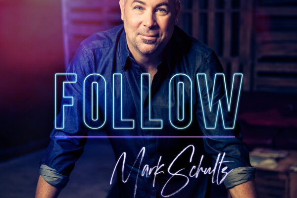 Man in dark shirt, leaning forward, with Follow text overlay. Dimly lit setting, colorful lighting effect.