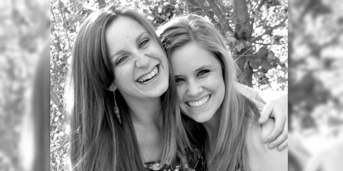 Two women smiling and hugging outdoors on a sunny day, black and white photo, highlighting friendship and joy.
