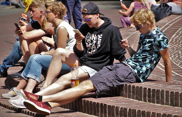 Young adults sitting outside using smartphones, enjoying sunny weather.