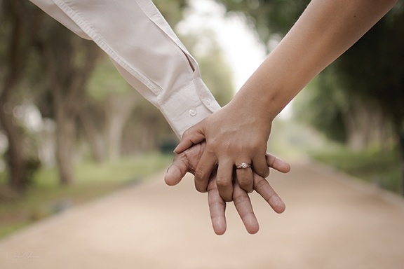 Two people holding hands with an engagement ring in a park setting, symbolizing love and commitment.