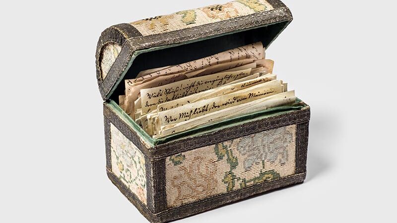 Antique box with intricate fabric design, open to reveal historical letters.