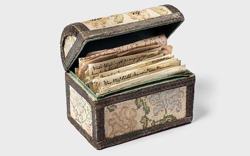 Antique box with intricate fabric design, open to reveal historical letters.