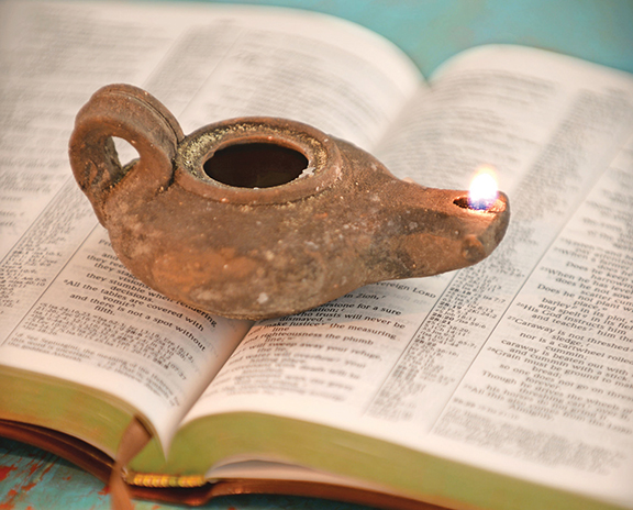 Ancient clay oil lamp burning on an open Bible, symbolizing enlightenment and knowledge.