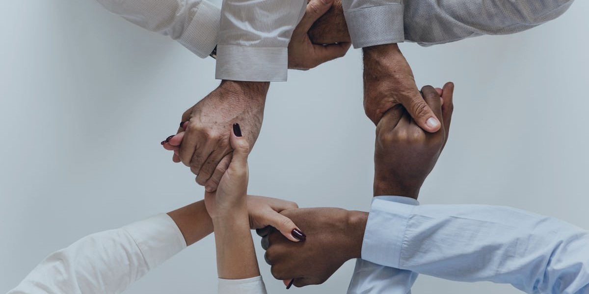 Diverse group of hands joined together symbolizing teamwork and unity against a neutral background.
