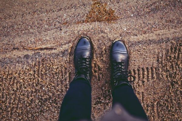 Black boots on sandy beach with visible texture and footprints, person standing on sand.